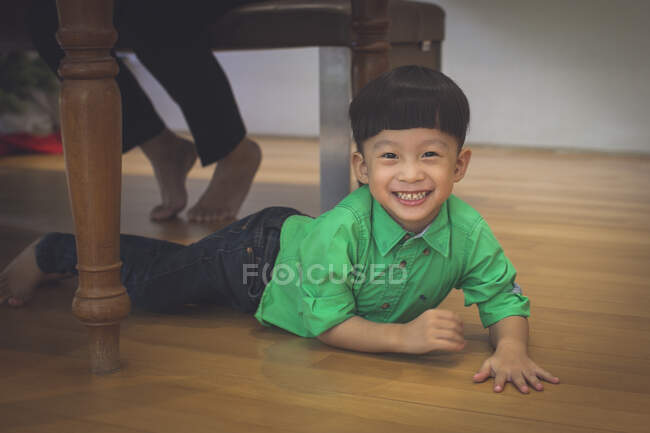 Menino brinca às escondidas debaixo da mesa enquanto janta — Fotografia de Stock