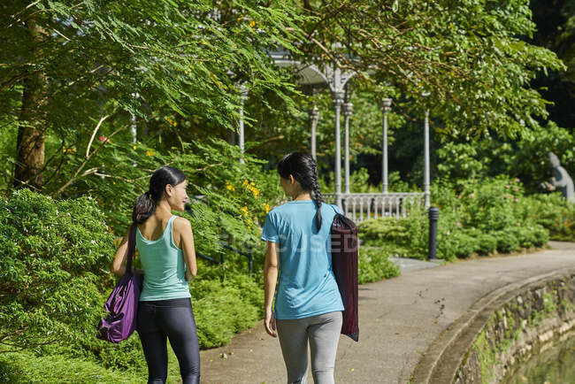 LEITUNGEN Zwei Frauen zu Fuß zu ihrem Yoga-Standort im Botanischen Garten in Singapur — Stockfoto