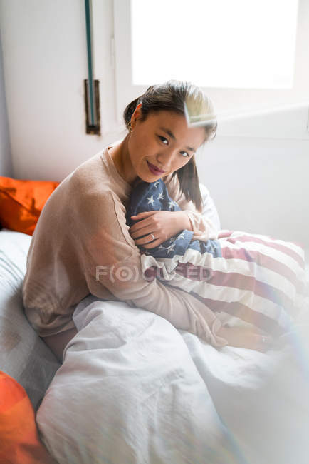 Jeune attrayant asiatique femme tenant drapeau américain oreiller — Photo de stock