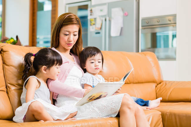Madre e hijos leyendo juntos en casa - foto de stock