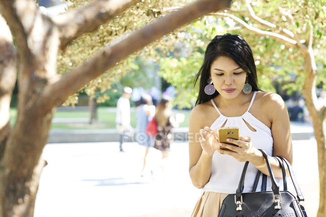 Bella donna malese al parco con il suo cellulare — Foto stock