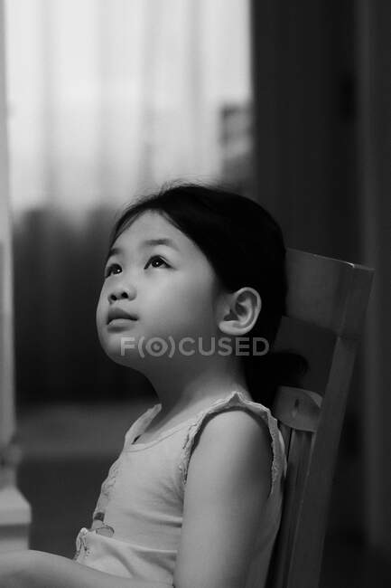 Linda criança sonhando acordado, sentado em uma cadeira e olhando para longe da câmera — Fotografia de Stock