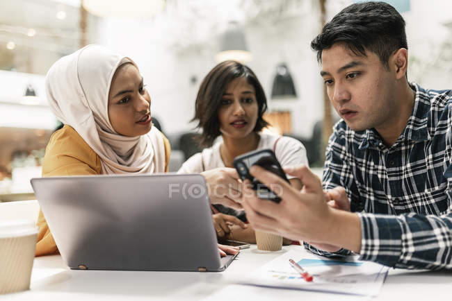 Young multicultural business people looking at smartphone in modern office — Stock Photo