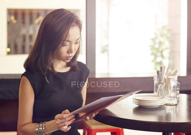 Joven hermosa mujer asiática mirando menú en la cafetería - foto de stock