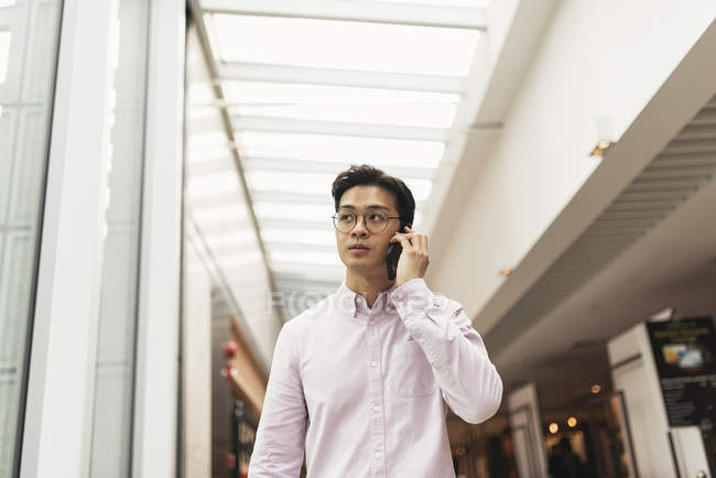 Молодой случайный азиатский человек, использующий умный в торговом центре — стоковое фото