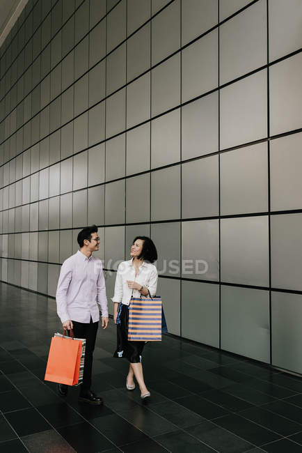 Young casual asian couple with bags at shopping in mall — Stock Photo