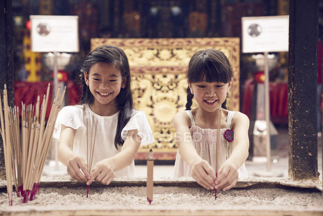 Две молодые азиатские девушки ставят свечи в святилище — стоковое фото