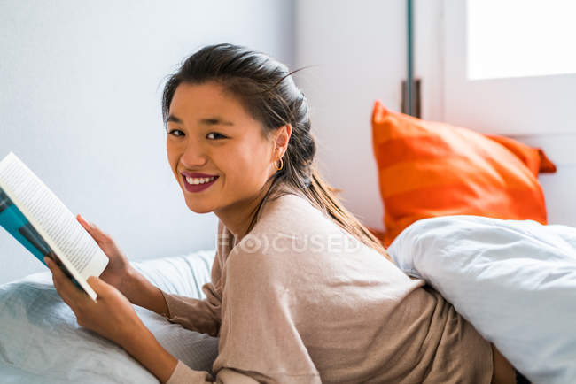 Junge attraktive asiatische Frau lesen Buch im Bett — Stockfoto