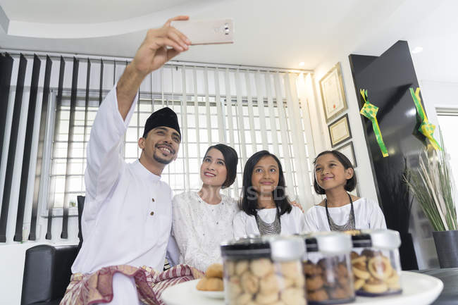 Jovem asiático família celebrando hari raia juntos no casa e tomando selfie — Fotografia de Stock
