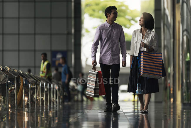 Young casual asian couple with bags at shopping in mall — Stock Photo