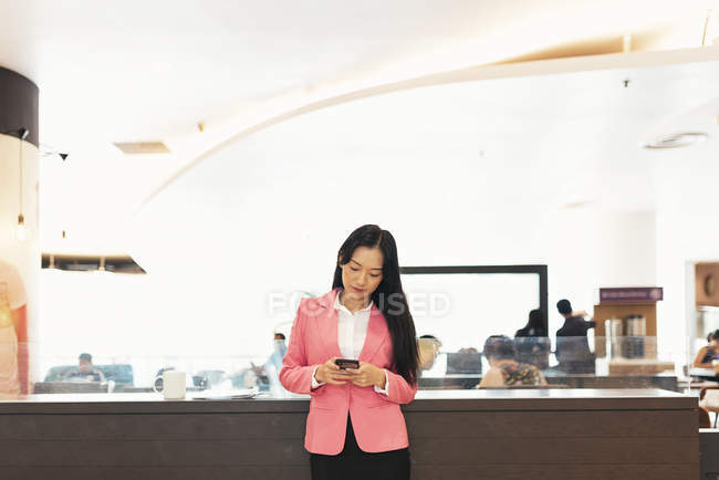 Junge attraktive asiatische Frau mit Smartphone in Einkaufszentrum — Stockfoto