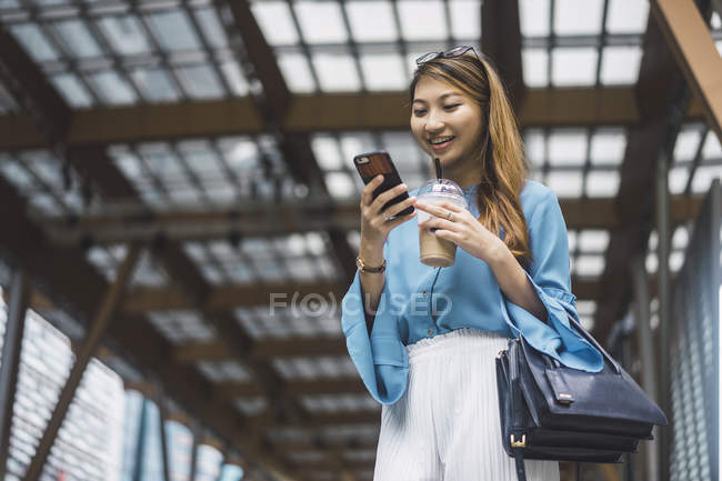 Atraente jovem asiático menina usando smartphone e café xícara — Fotografia de Stock