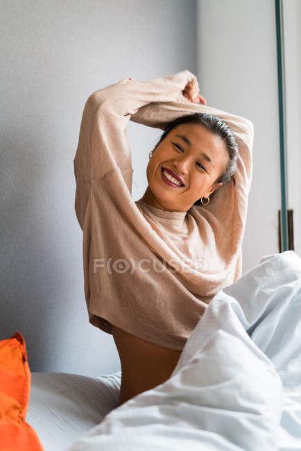 Junge attraktive asiatische Frau mit erhobenen Armen im Bett — Stockfoto
