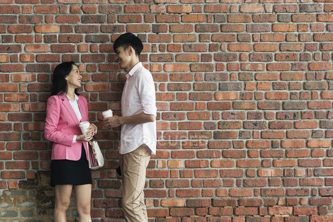 Atractivo joven asiático pareja de pie por la pared con tazas de café - foto de stock