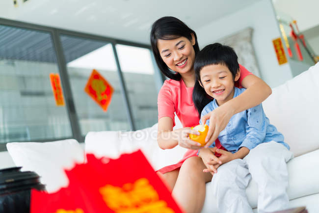 Счастливая азиатская семья вместе, мать держит оранжевые фрукты для сына — стоковое фото