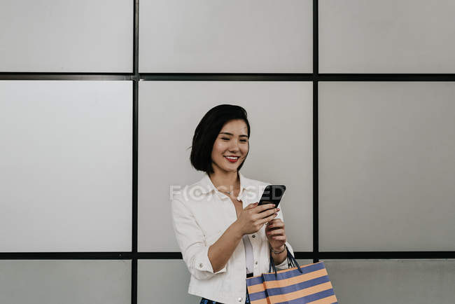 Молодая случайная азиатка, использующая смартфон в торговом центре — стоковое фото