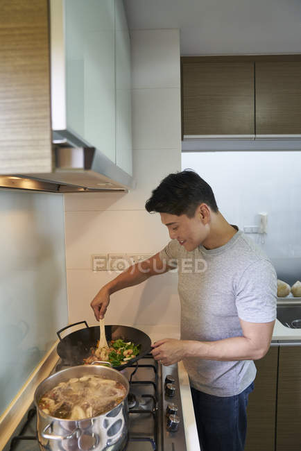 Feliz asiático hombre cocina comida en cocina - foto de stock