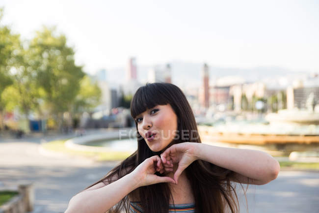 Jeune eurasiatique femme montrant coeur avec doigts à caméra — Photo de stock