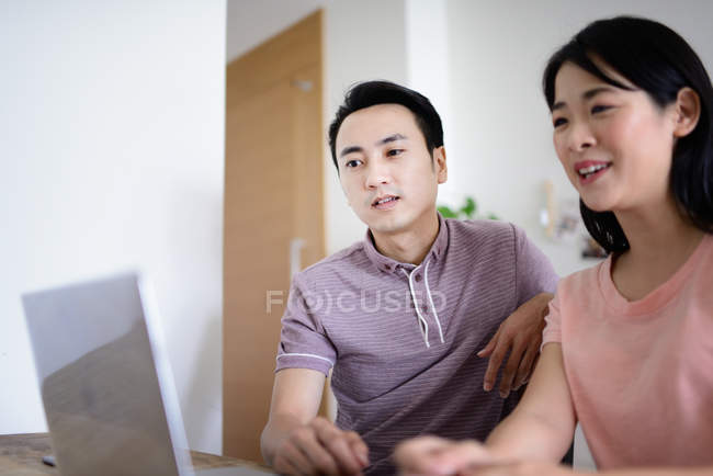 Madura asiática casual pareja trabajando con laptop en casa - foto de stock