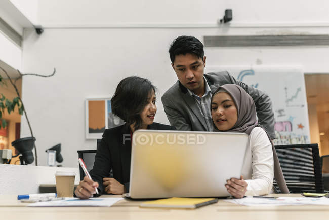 Jovens empresários multiculturais que trabalham com laptop em escritório moderno — Fotografia de Stock