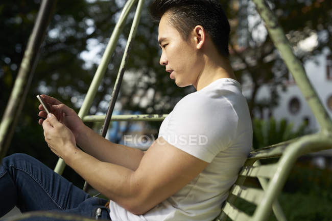 Mann benutzt sein Handy auf einer Schaukel im Tanjong Pagar, Singapore — Stockfoto