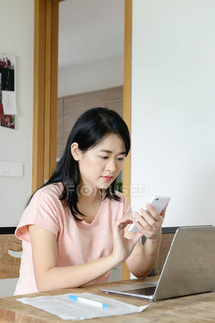 Молодая случайная азиатская женщина, использующая смартфон дома — стоковое фото