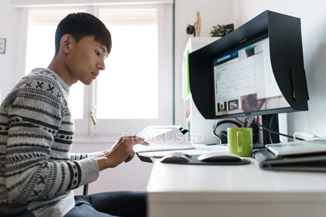 Молодой азиат работает дома, вид сбоку — стоковое фото