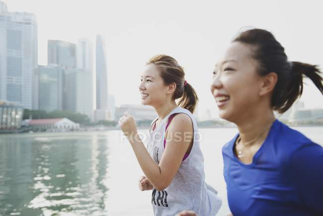 Dos mujeres deportivas corriendo al aire libre contra el agua - foto de stock