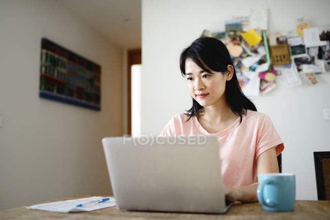 Young casual asian woman using laptop at home — Stock Photo