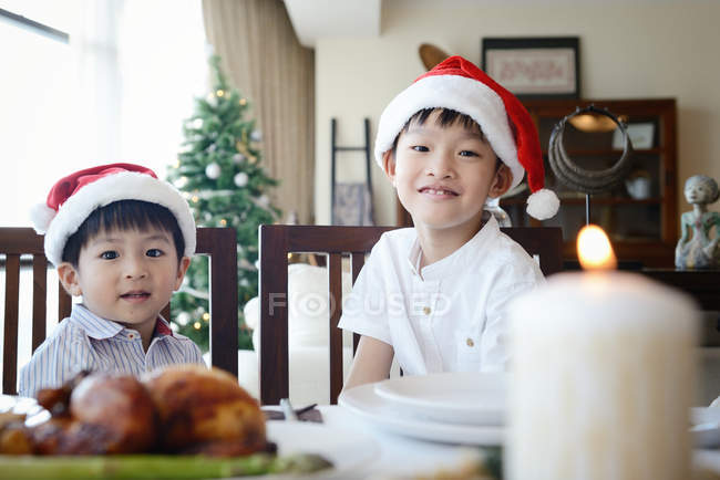 Familia asiática celebrando las vacaciones de Navidad, dos hermanitos en la mesa - foto de stock