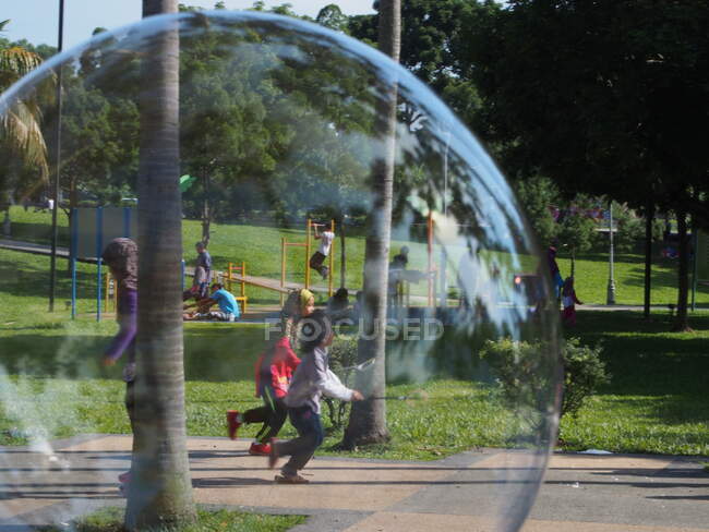Soap bubble coincidentally framing kids having fun in the park. — Stock Photo