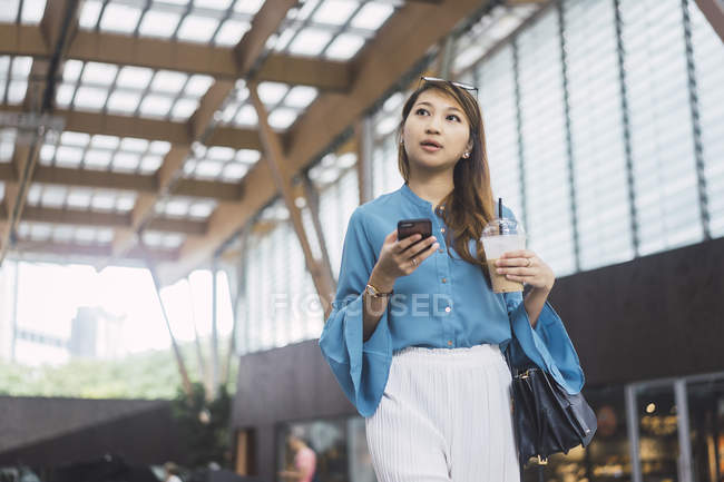 Atractivo joven asiático chica usando smartphone y café taza - foto de stock