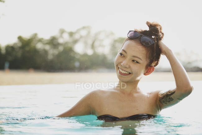 Primer plano vista de feliz hermosa mujer asiática nadando en piscina - foto de stock
