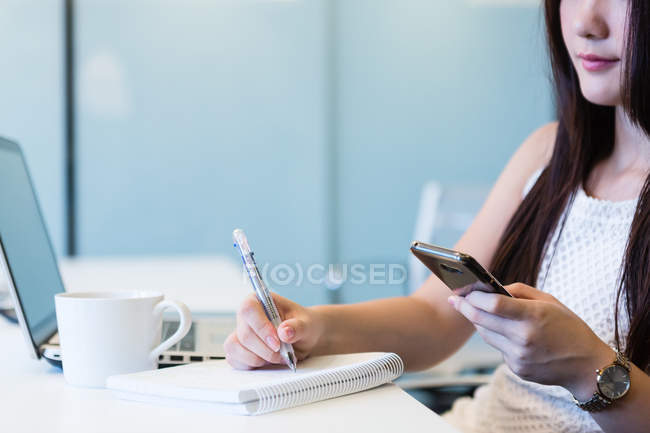 Крупним планом молода жінка робить нотатки з її телефону . — стокове фото