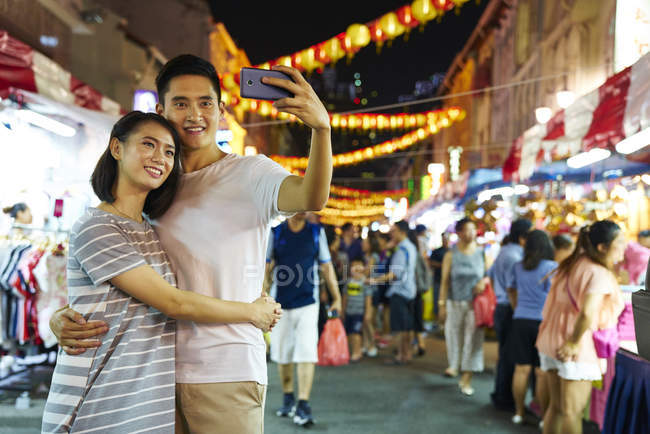 Young asian couple spending time together on traditional bazaar at Chinese New Year and taking selfie — Stock Photo