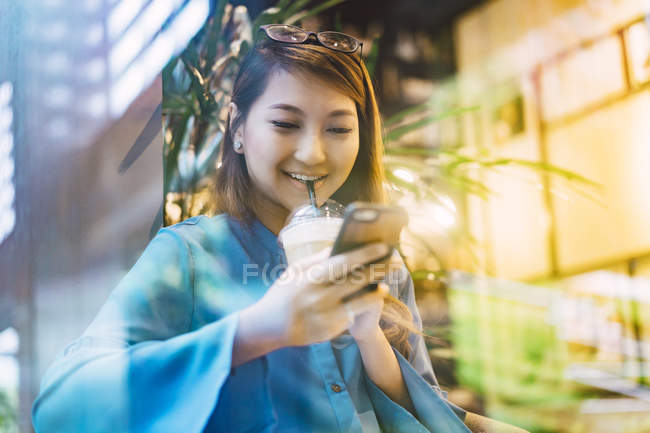Atraente jovem asiático menina usando smartphone e café xícara — Fotografia de Stock