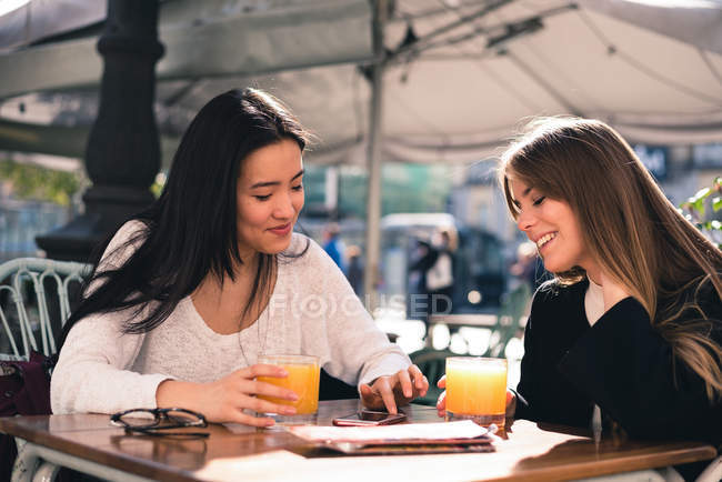 Hermosos amigos con un teléfono inteligente en las calles de España sentados en una cafetería - foto de stock