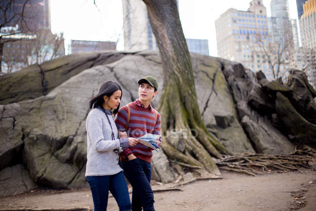 Turistas asiáticos caminhando com mapa contra árvores — Fotografia de Stock
