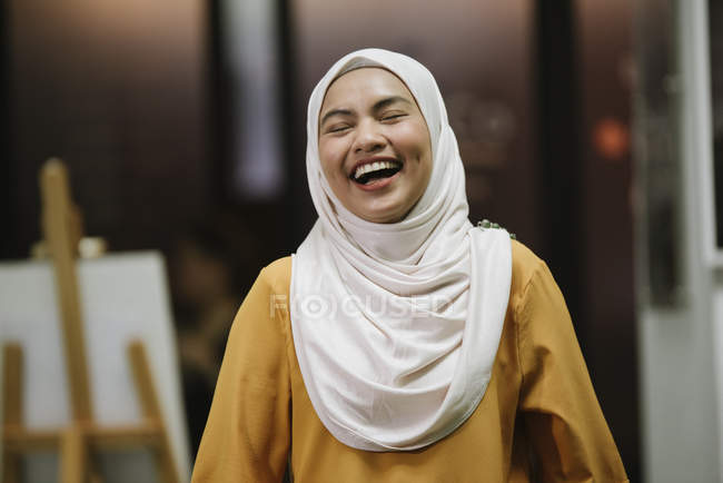 Joven asiático negocios mujer en hijab riendo en moderno oficina - foto de stock