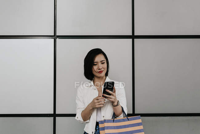 Giovane donna asiatica casuale utilizzando smartphone al centro commerciale — Foto stock