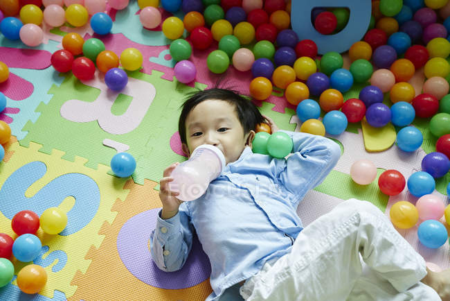 Toddler drinking from a milk bottle in a play pen — Stock Photo