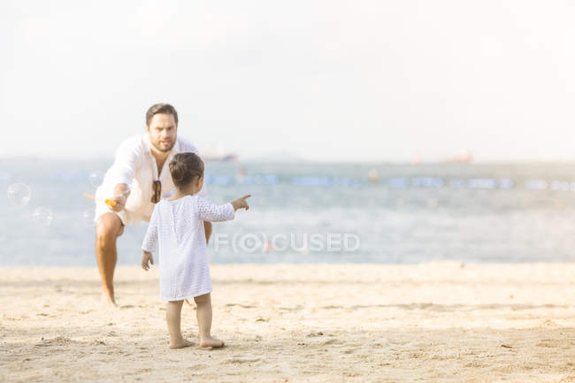 Heureuse famille caucasienne sur la plage, petite fille pointant sur quelque chose — Photo de stock