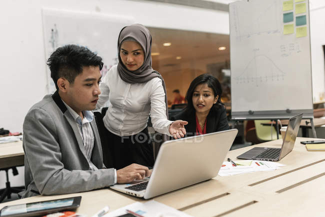 Gente joven de negocios multiculturales que trabajan con el ordenador portátil en la oficina moderna - foto de stock