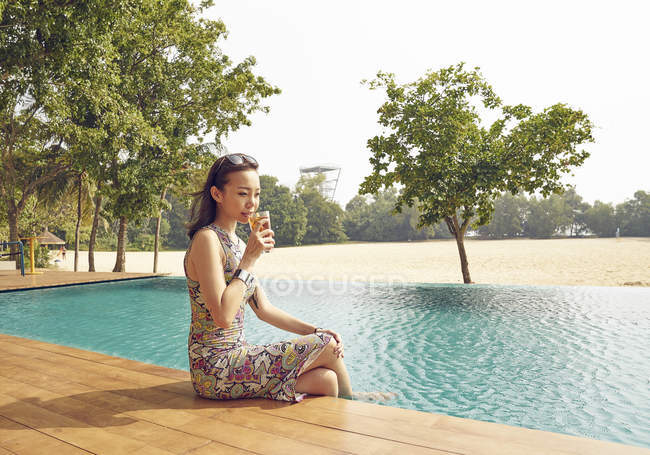 Young beautiful asian woman drinking beverage near pool — Stock Photo