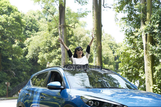 Young woman standing through the opening of a sun roof on a car — Stock Photo