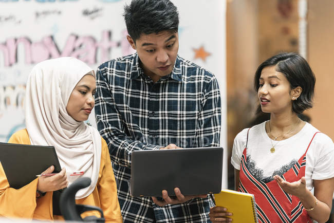 Jovens empresários multiculturais que compartilham laptop no escritório moderno — Fotografia de Stock