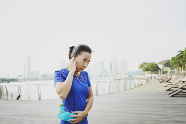 Young sporty asian woman with earphones at pier — Stock Photo