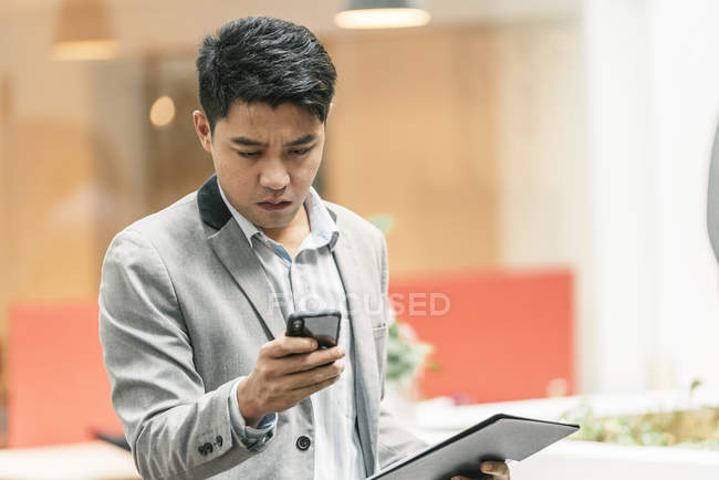 Jeune homme d'affaires asiatique en utilisant smartphone dans le bureau moderne — Photo de stock