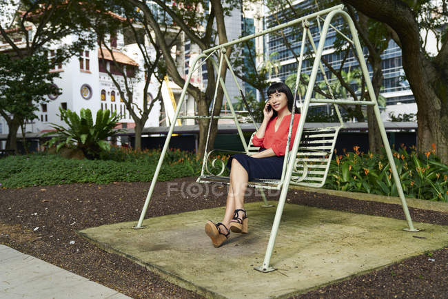 Jovencita usando su celular en el parque, Singapur - foto de stock