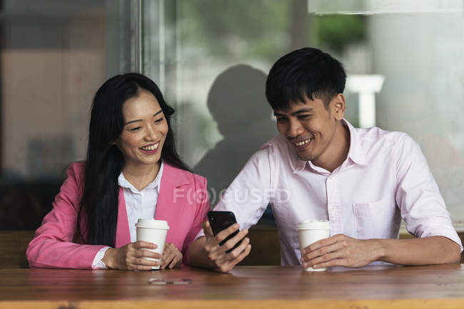 Attractive young asian couple drinking coffee and using smartphone — Stock Photo